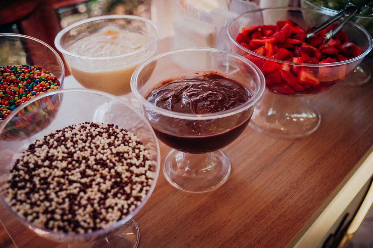 Taças de vidro com caldas de chocolate, morangos picados e confeitos