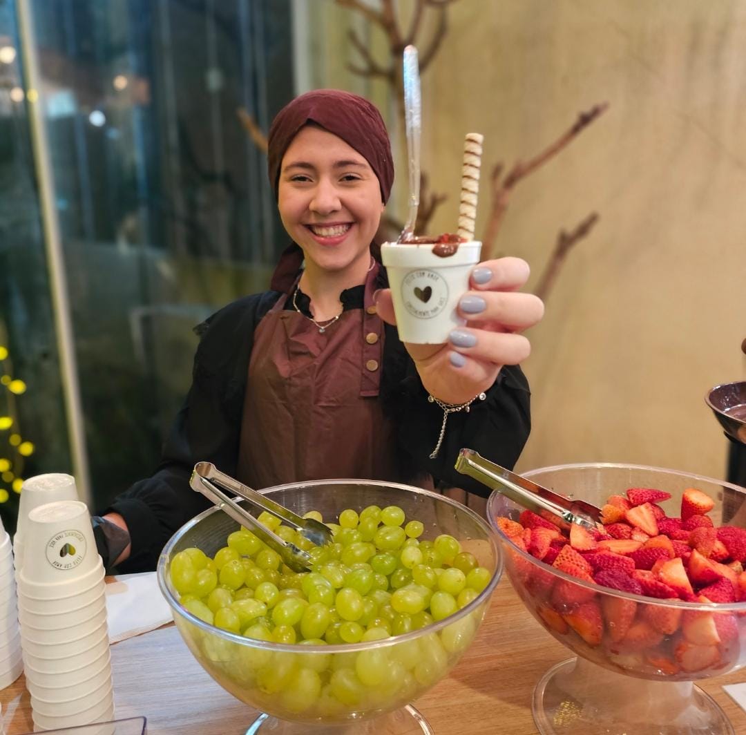 Atendente sorridente da VM Estações Gourmet servindo um copinho de sobremesa na estação de fondue