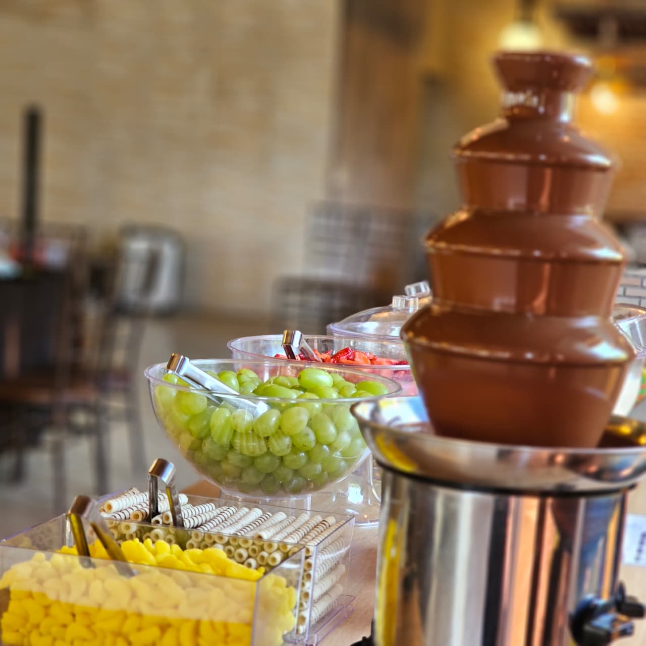 Cascata de chocolate da estação de fondue com taças de frutas e acompanhamentos